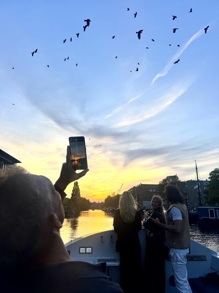 This photo captures a serene evening on the Entrepotdok, Kadijken, Amsterdam, as people on a canal boat enjoy a vibrant sunset